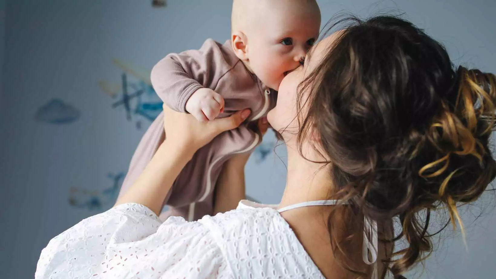 Brunette woman seen from behind holding a baby to her face and smiling
